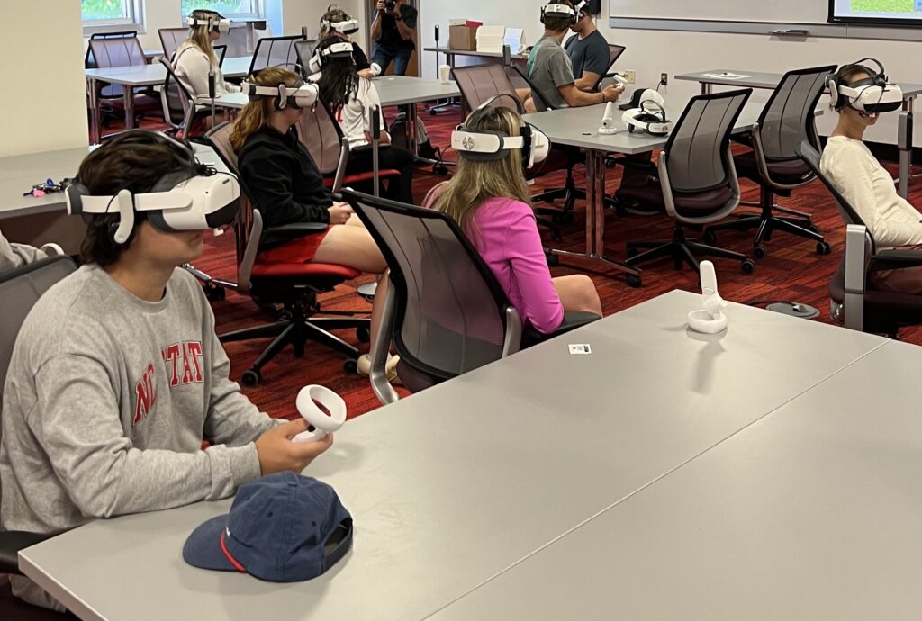 Classroom of students with virtual reality headsets on, sitting and viewing recordings
